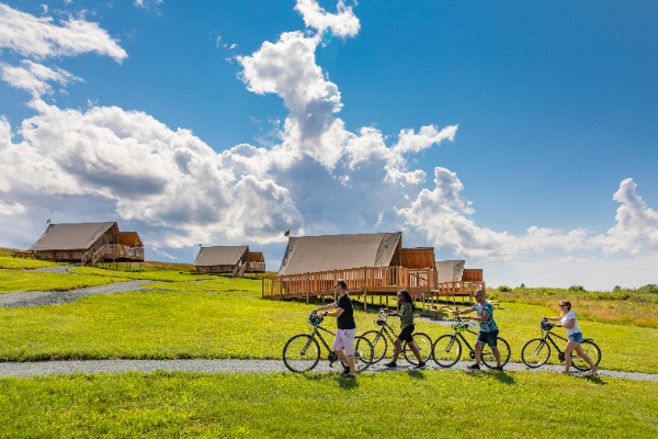 Family walking bikes along a trail with cabins in background
